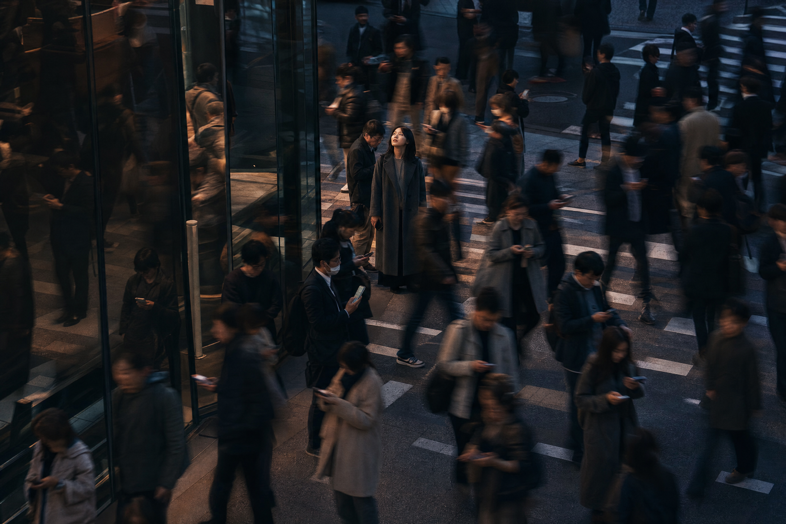 A crowd crosses a city street while one person lowers a phone and looks toward the sky.