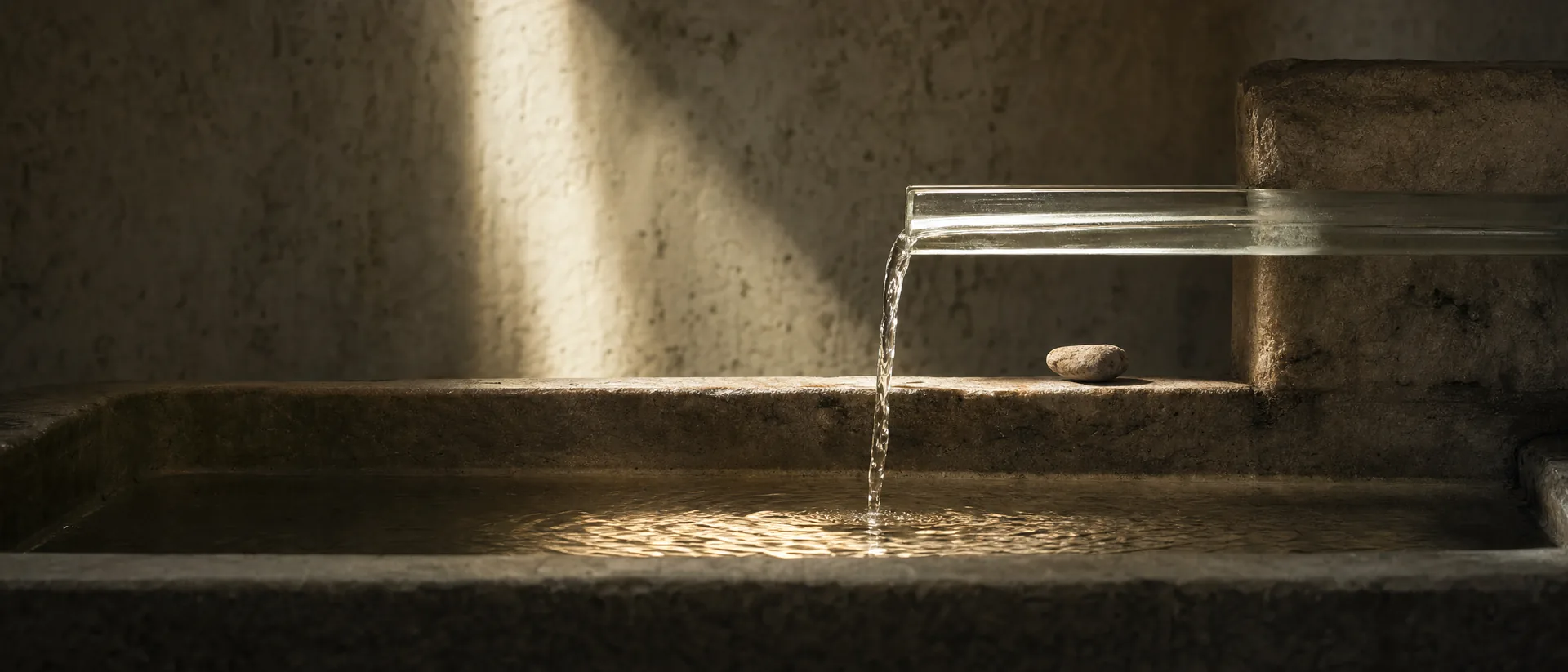 A narrow channel of clear water entering a stone basin beside a small mineral stone